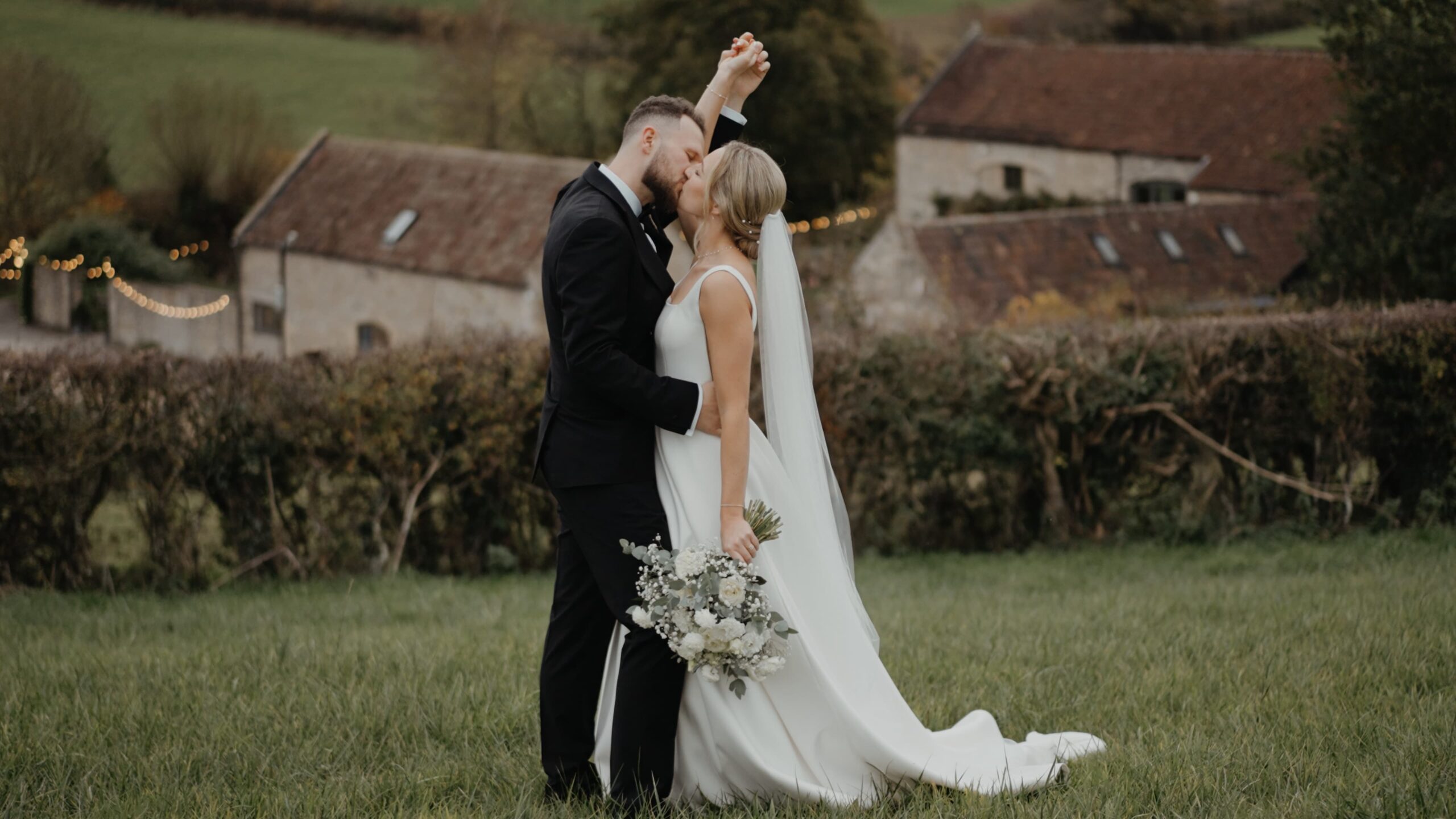 Couple sharing a kiss at golden hour outside Priston Mill, captured in a cinematic wedding film with soft countryside backdrop and natural wedding videography style