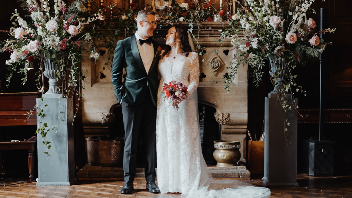 Bride and groom standing by a floral fireplace inside Huntsham Court, a historic Devon wedding venue, captured in a cinematic Devon wedding film
