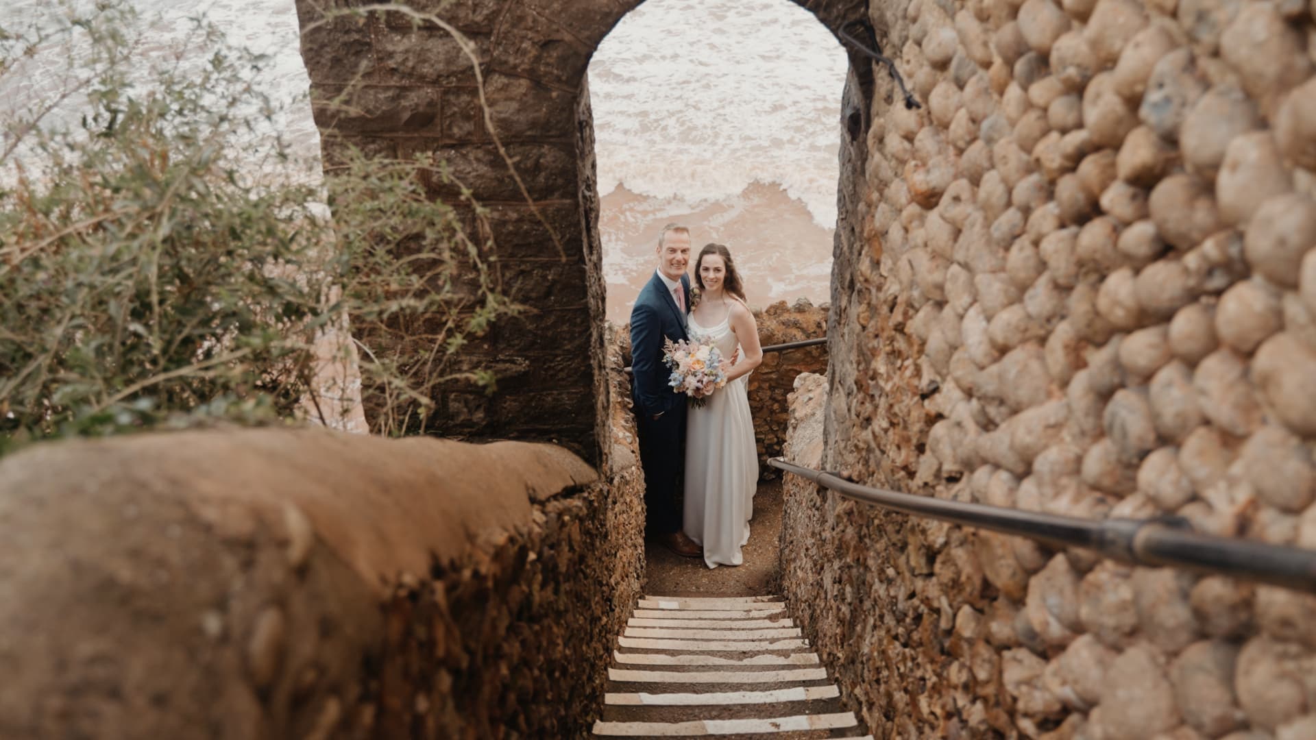 Bride and groom framed by a stone archway at Sidmouth Harbour Hotel, a Devon coastal wedding venue, captured by a Devon wedding filmmaker