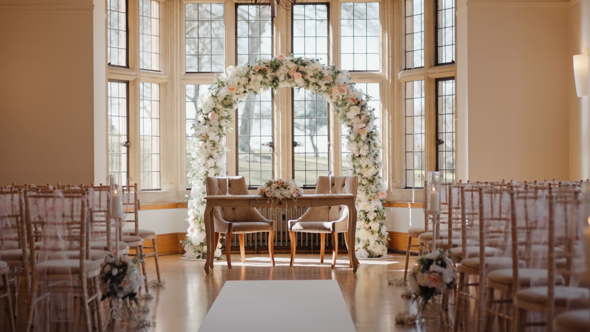 Elegant ballroom setup at Coombe Lodge Blagdon featuring a beautiful floral arch, pink flower arrangements and sophisticated wedding styling details.
