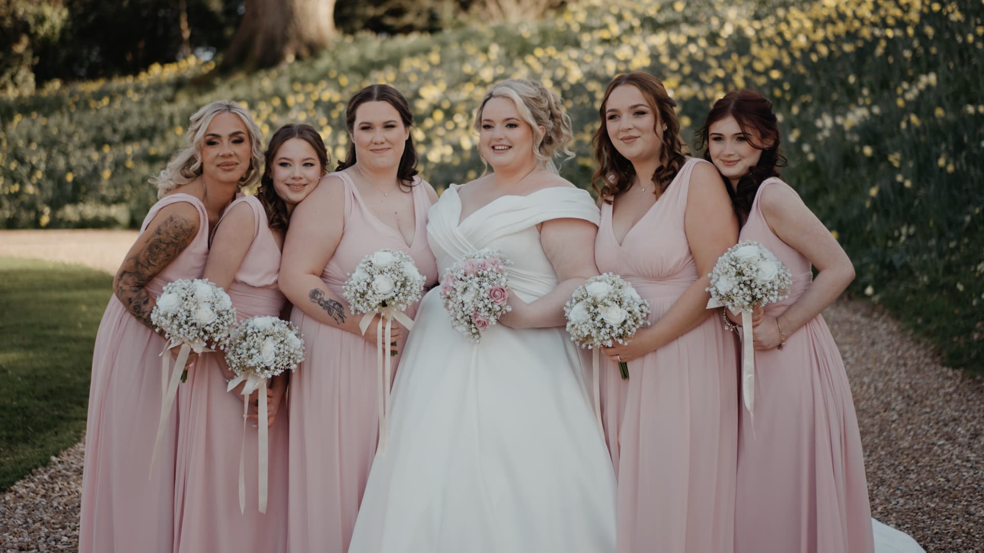 Bride posing with her bridesmaids wearing pink dresses against the picturesque Coombe Lodge Blagdon landscape during a stylish Somerset wedding.