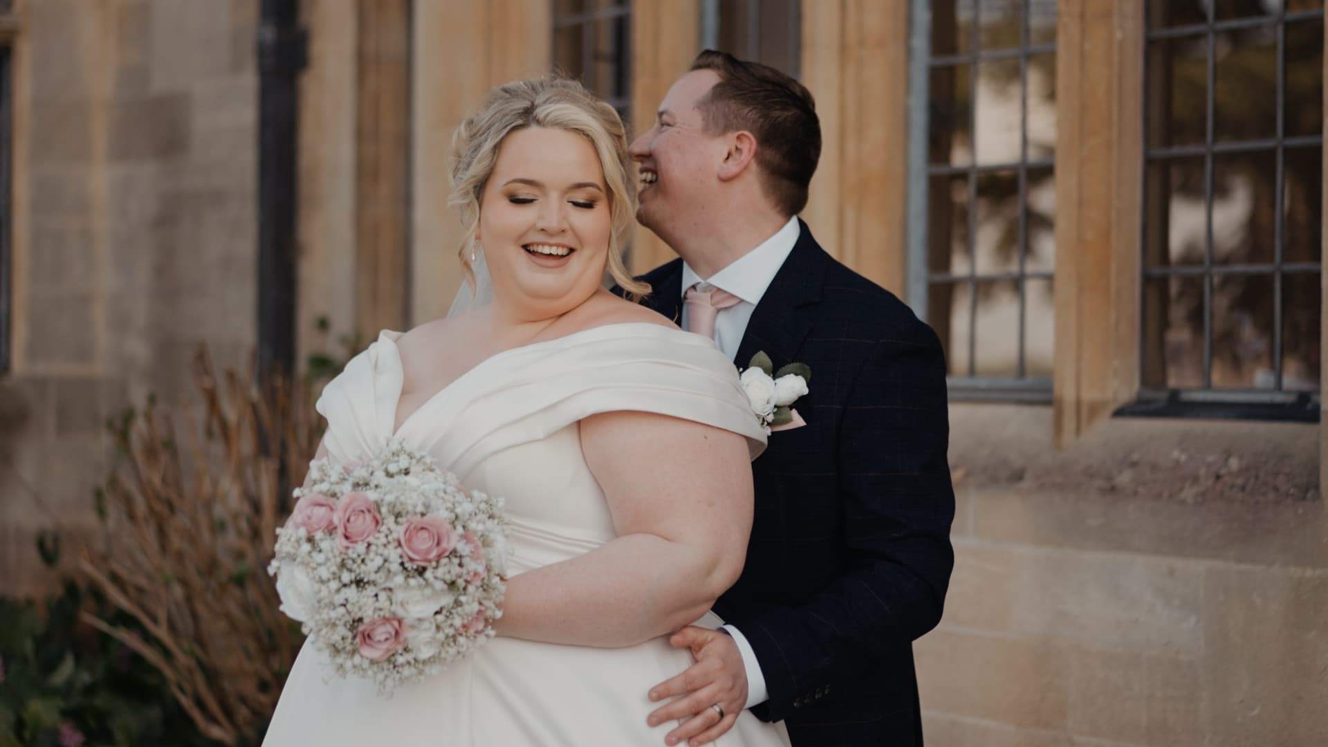 Groom backhugging his bride holding her bouquet in front of the stunning Coombe Lodge Blagdon architecture, creating a romantic portrait during their Somerset wedding.