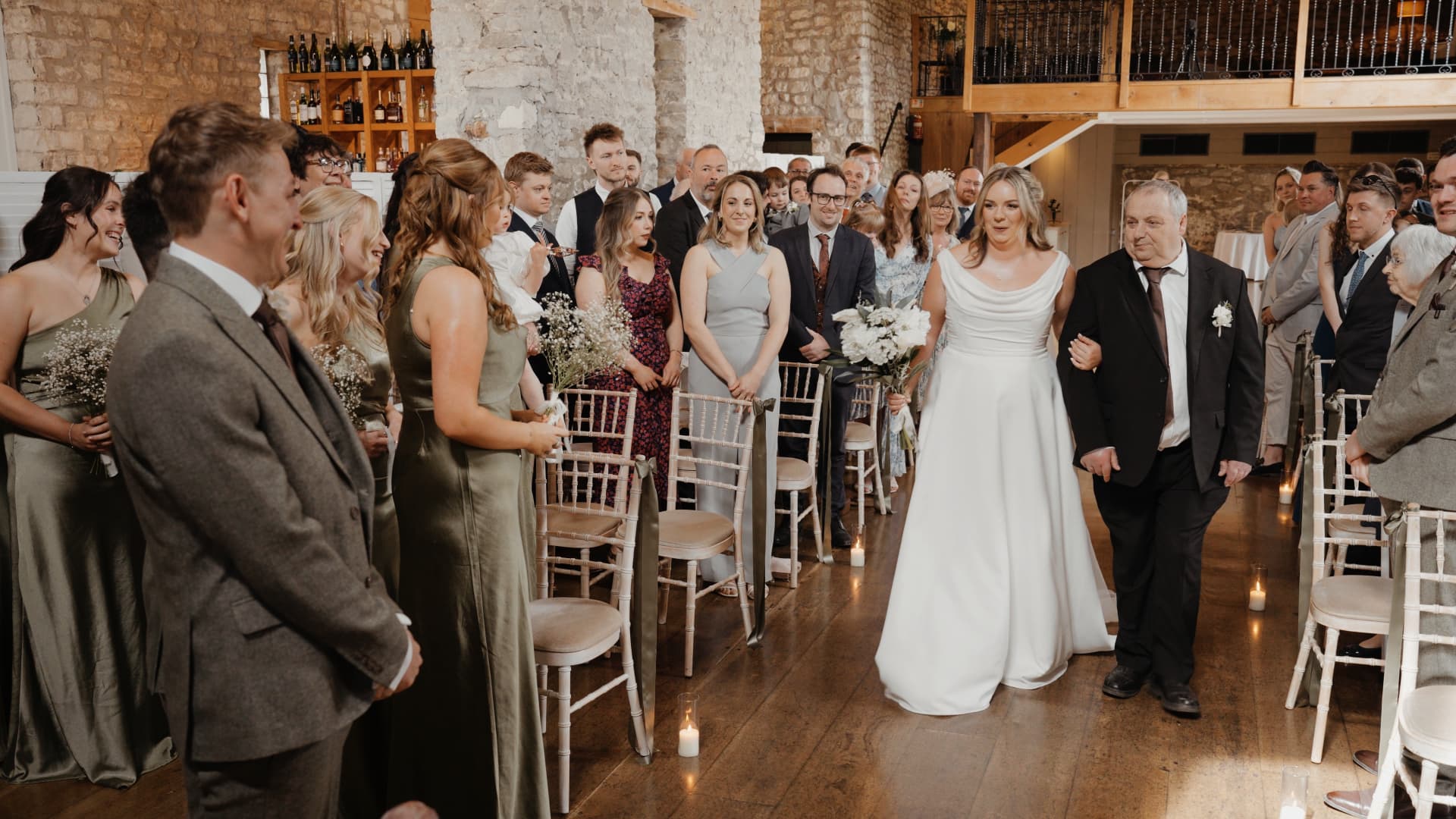 Bride smiling at her groom as he waits at the end of the aisle during their wedding at Priston Mill.