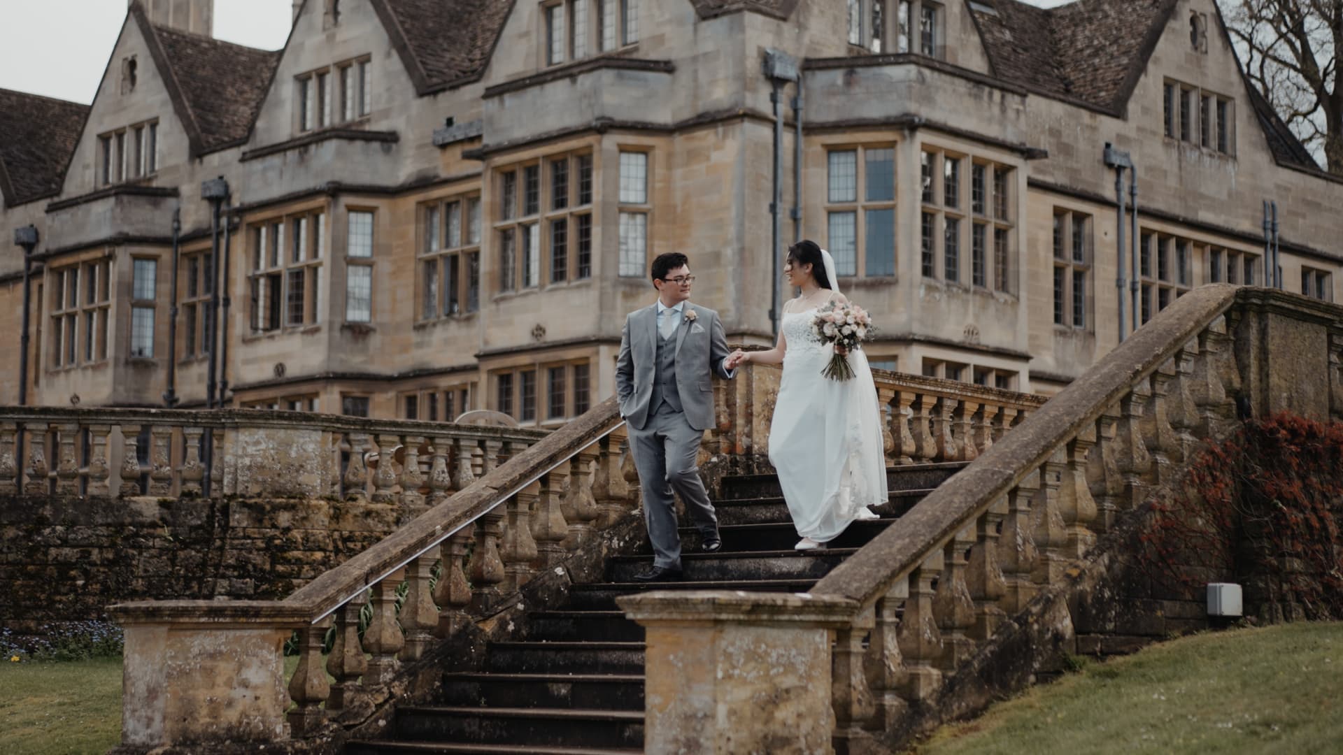 Bride and groom walking down the historic stone steps at Coombe Lodge, with the elegant Somerset wedding venue and landscaped grounds behind them.