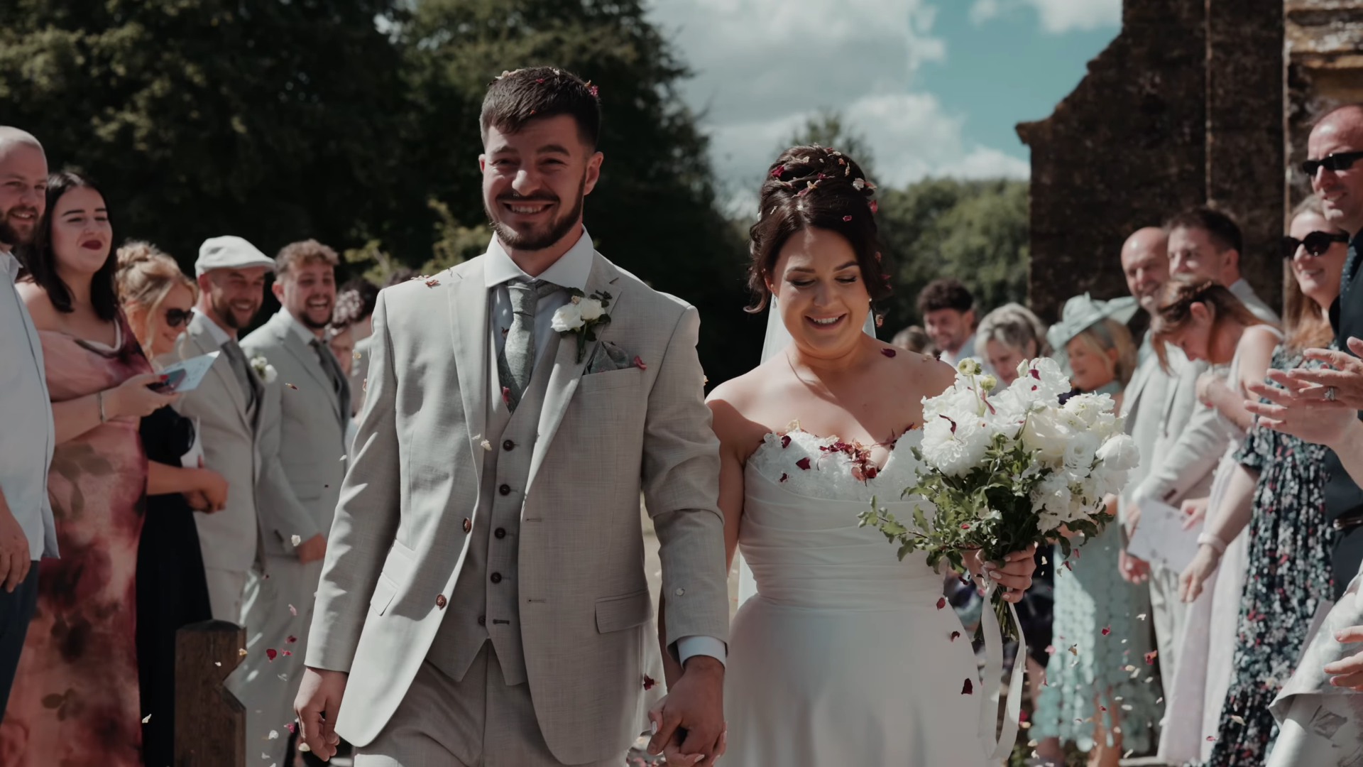 Bride and groom walk through a confetti exit outside St George's Church in Hinton St George, Somerset