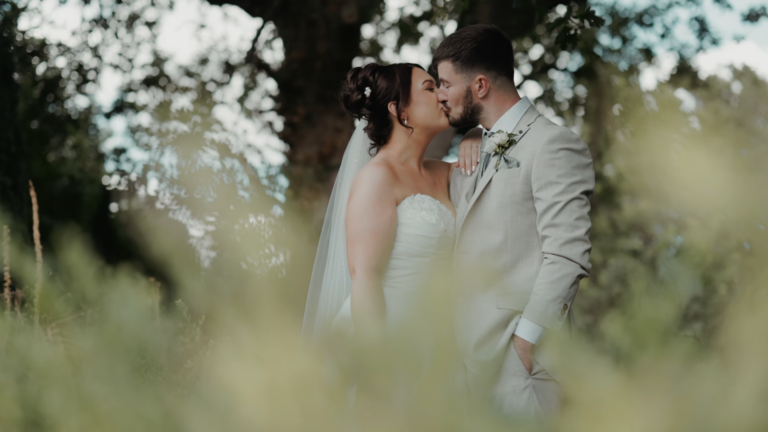 Aimee and Luke kiss beneath the trees in a cinematic Somerset wedding film still