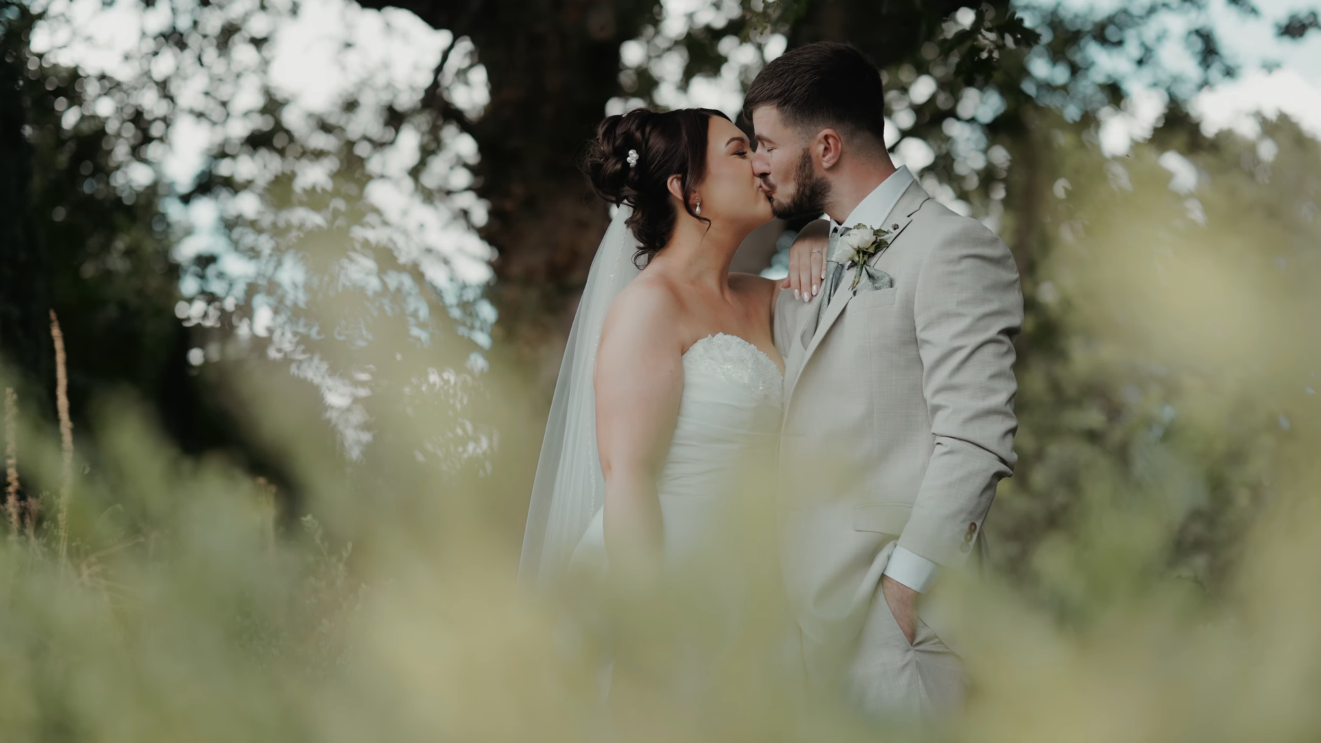 Aimee and Luke kiss beneath the trees in a cinematic Somerset wedding film still